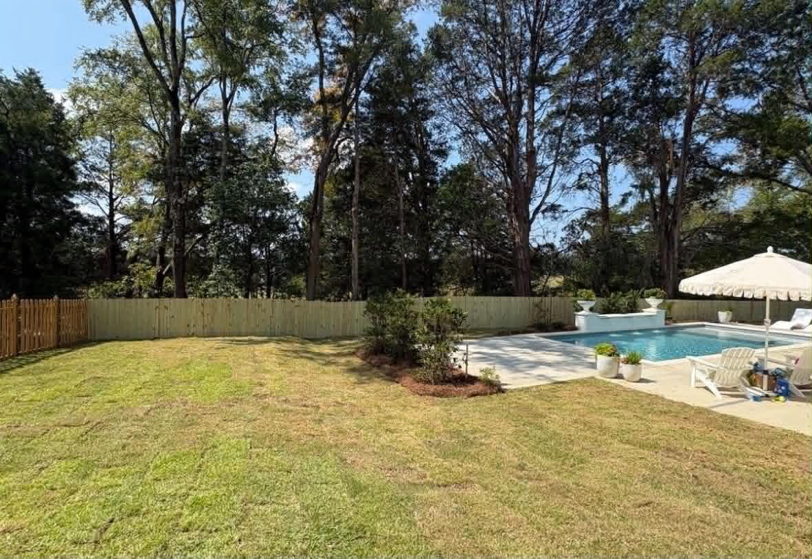 After: the same poolside backyard with new sod and a mulched island bed